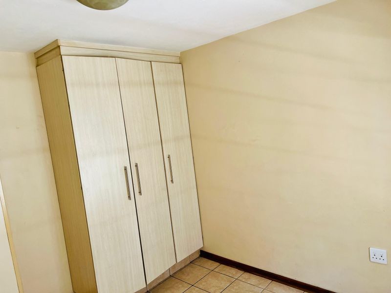 A simple bedroom featuring a light wood-finish built-in wardrobe, tiled flooring, and neutral wall tones, offering a clean and functional space.