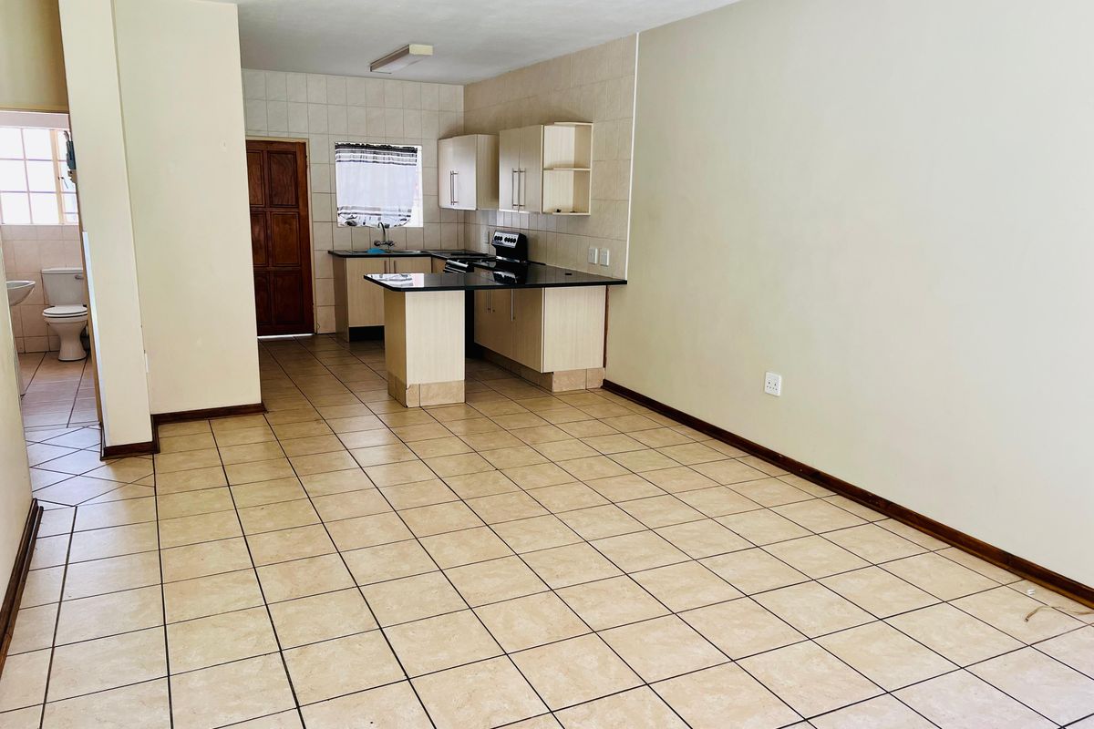 Open-plan living area featuring tiled flooring and a functional kitchen with granite countertops, built-in cabinetry, and a stove, leading to an adjacent bathroom.