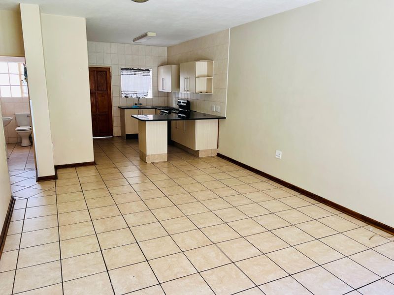 Open-plan living area featuring tiled flooring and a functional kitchen with granite countertops, built-in cabinetry, and a stove, leading to an adjacent bathroom.