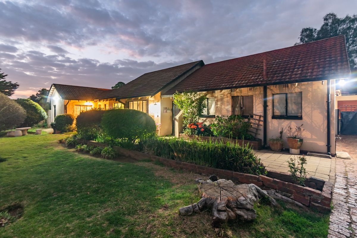 A rear view of the house featuring a paved patio area, a well-maintained lawn, and a tiled roof at dusk.