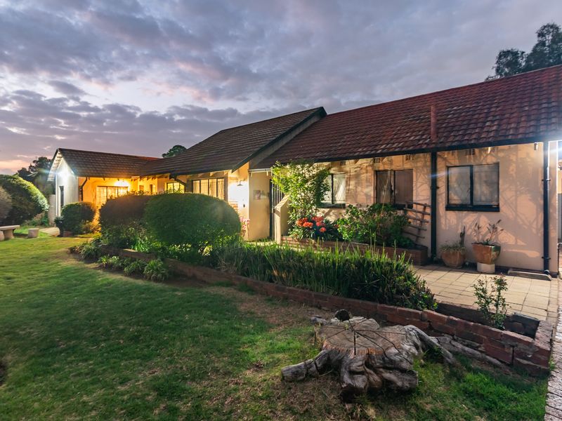 A rear view of the house featuring a paved patio area, a well-maintained lawn, and a tiled roof at dusk.