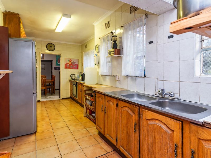 A functional kitchen featuring traditional wooden cabinetry, double basin stainless steel sink, tiled splashbacks, and ceramic floor tiles, offering potential for modern renovation.