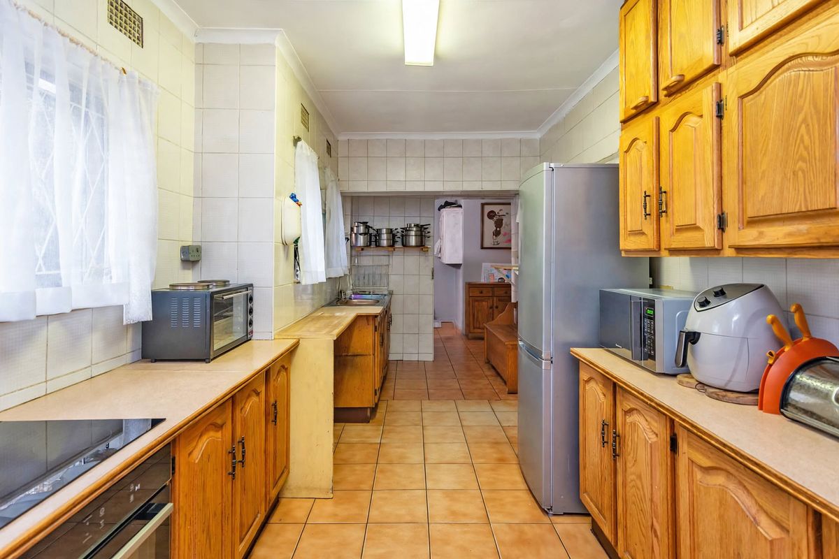 A functional kitchen featuring traditional wooden cabinetry, tiled walls, and ceramic flooring, offering a classic layout with ample storage and prep space.
