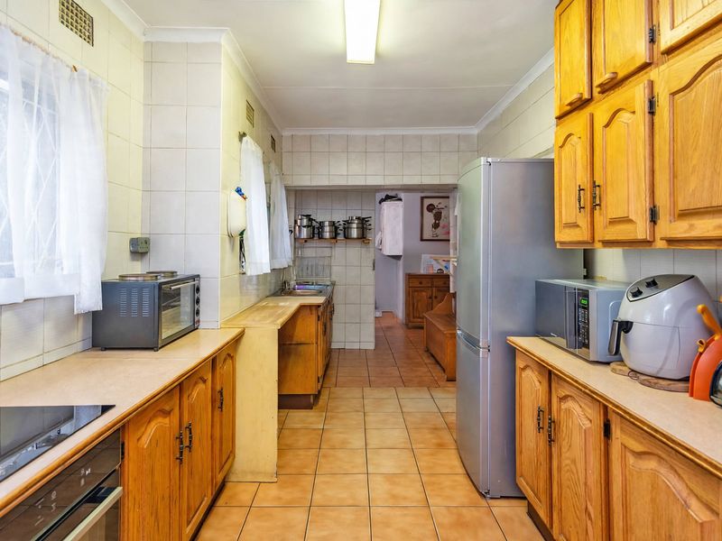 A functional kitchen featuring traditional wooden cabinetry, tiled walls, and ceramic flooring, offering a classic layout with ample storage and prep space.