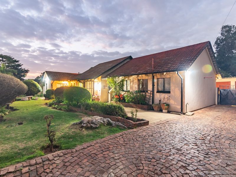 A charming single-story home featuring a tiled roof, cobblestone driveway, and well-maintained garden beds, captured during the golden hour.