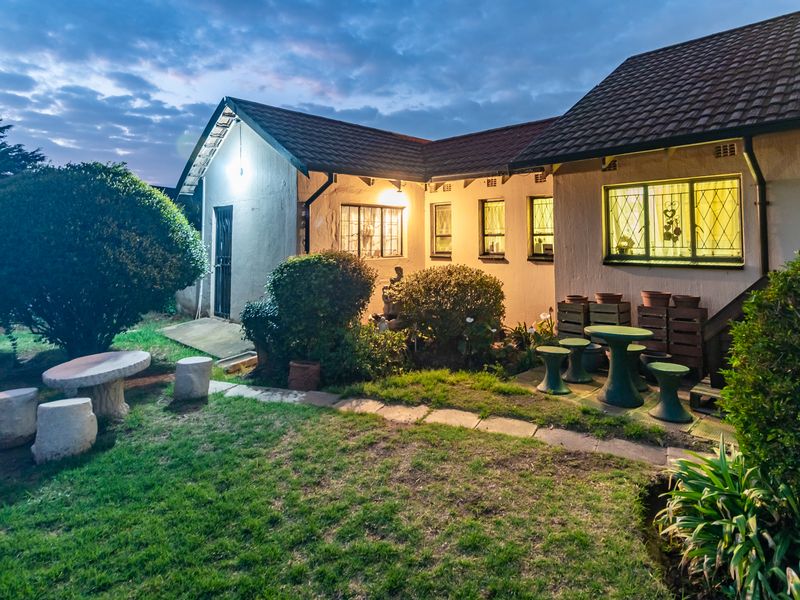 A rear view of the house at dusk, featuring a landscaped garden, tiled roof, and exterior lighting illuminating the facade.