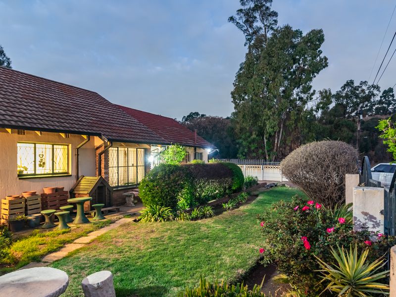 A view of the rear exterior of the house featuring a well-maintained garden, paved walkway, and secure window bars.