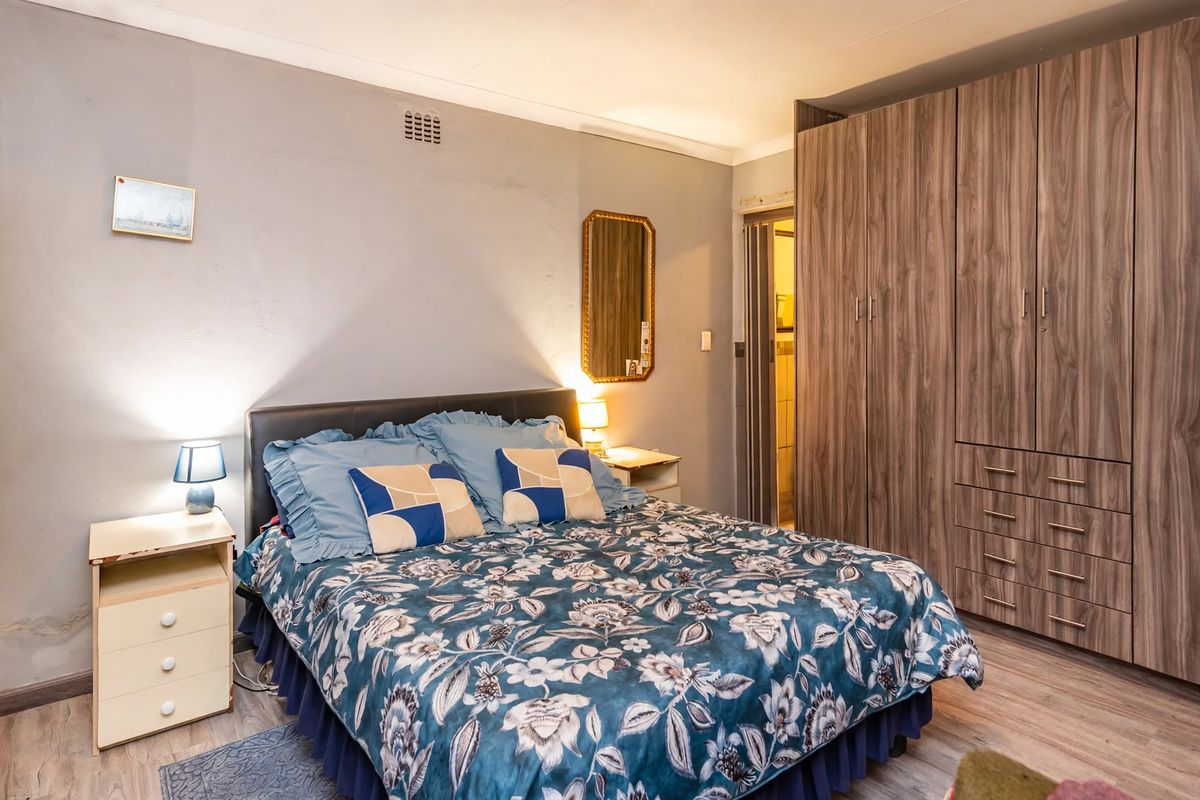 Bedroom featuring built-in wooden cupboards and laminate flooring. The room shows signs of wall surface deterioration requiring maintenance.