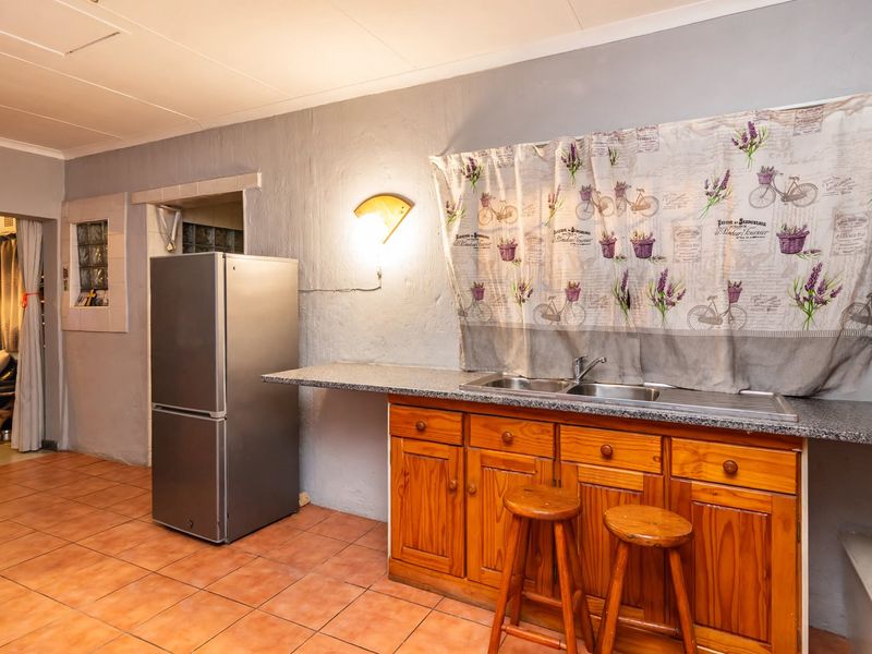 A functional kitchen area featuring wooden cabinetry, a stainless steel double sink, and ceramic floor tiles, offering potential for modernization.