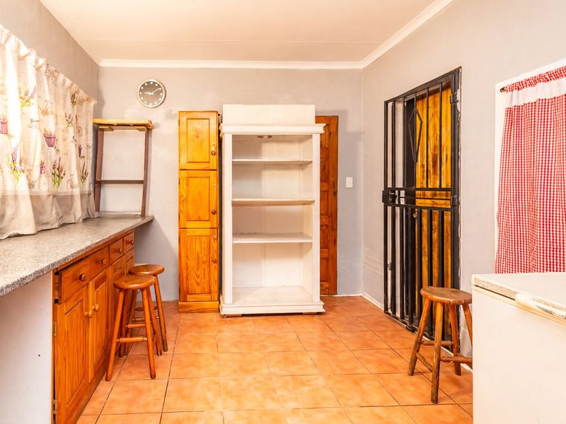 A functional kitchen area featuring wooden cabinetry, granite countertops, and tiled flooring, with a security gate leading to an exterior door.