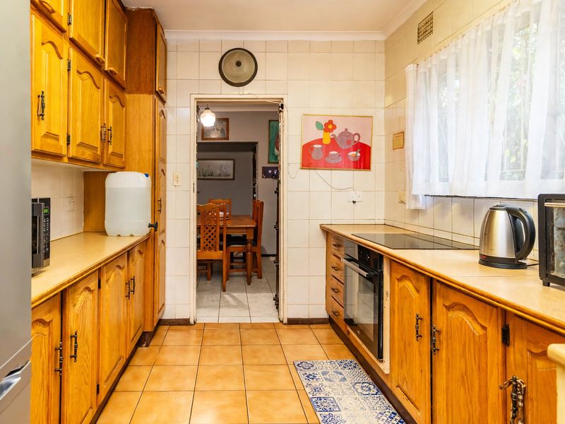 A functional galley-style kitchen featuring traditional wooden cabinetry, tiled walls, and built-in cooking appliances, offering a classic layout with potential for modern updates.