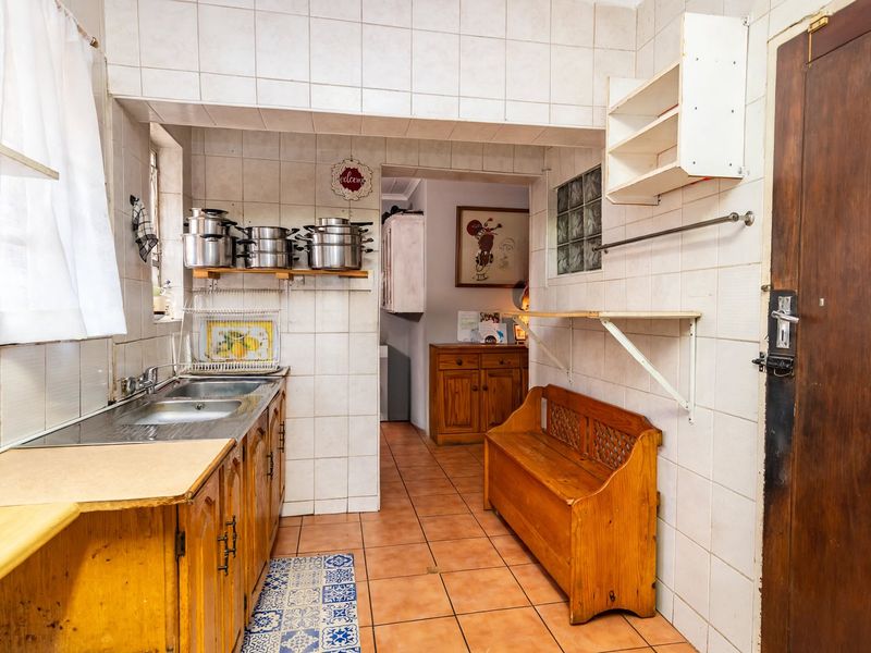 A functional kitchen featuring tiled walls and flooring, built-in wooden cabinetry, and a double stainless steel sink, offering potential for modern renovation.