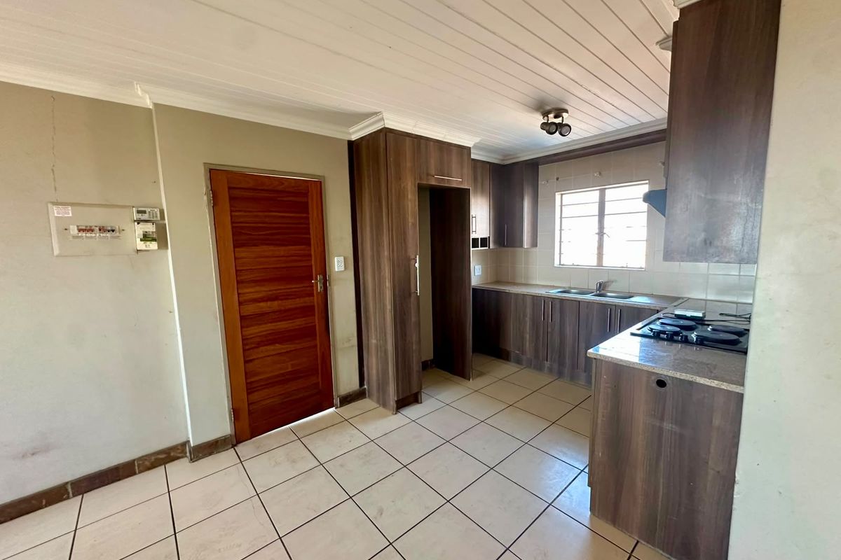 A functional kitchen featuring dark wood cabinetry, laminate countertops, a gas hob, and tiled flooring, with a timber-paneled ceiling.