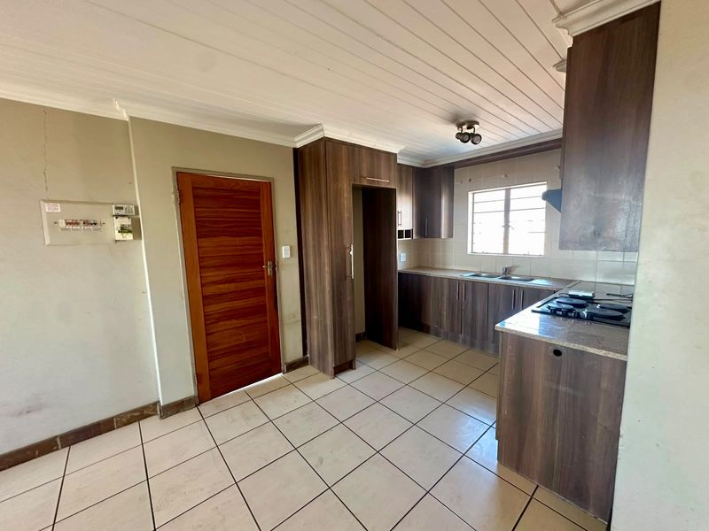 A functional kitchen featuring dark wood cabinetry, laminate countertops, a gas hob, and tiled flooring, with a timber-paneled ceiling.