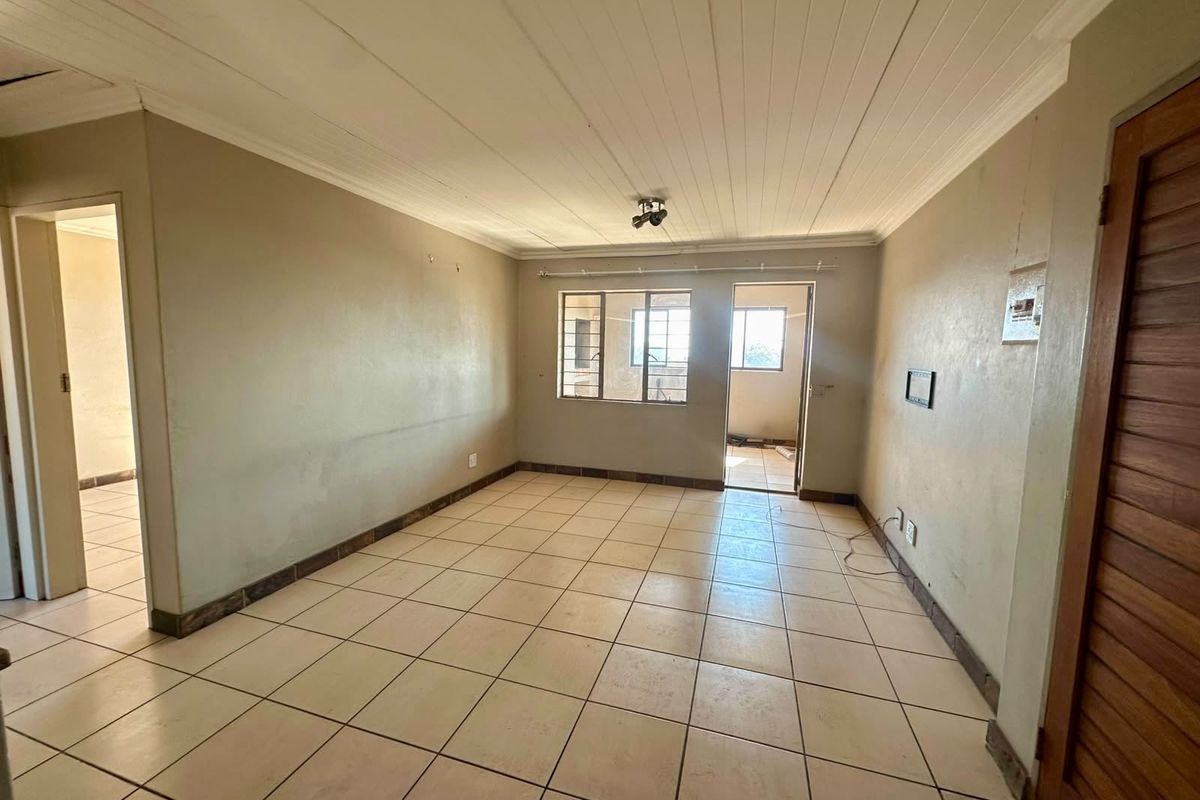 An empty, open-plan living area featuring tiled flooring, a timber ceiling, and steel-framed windows, offering a blank canvas for renovation.