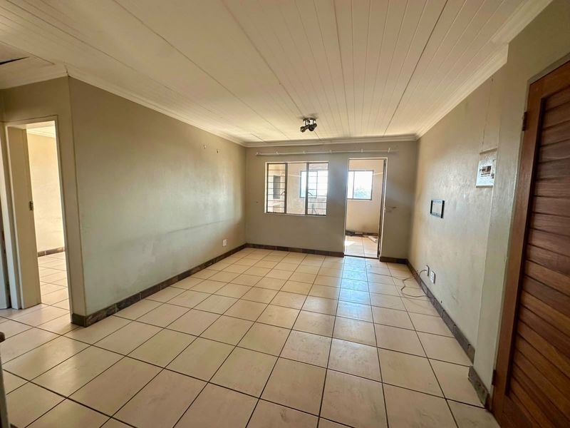 An empty, open-plan living area featuring tiled flooring, a timber ceiling, and steel-framed windows, offering a blank canvas for renovation.