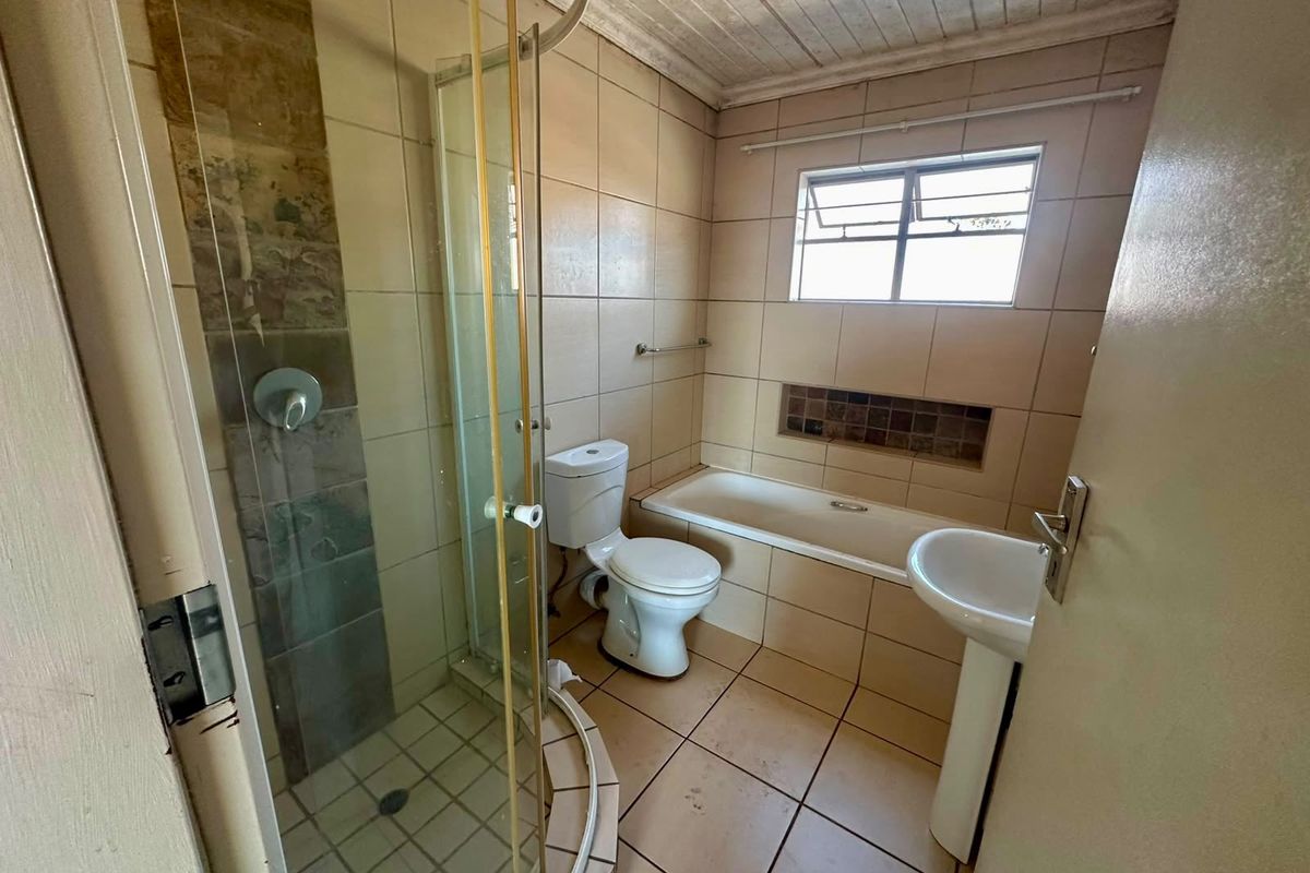 A dated bathroom featuring a shower enclosure, bathtub, pedestal basin, and toilet with neutral wall and floor tiling.