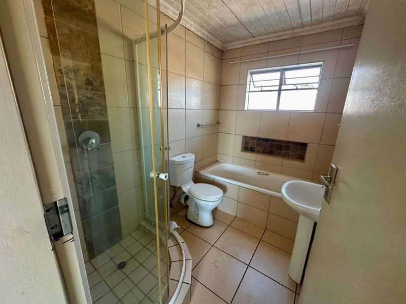 A dated bathroom featuring a shower enclosure, bathtub, pedestal basin, and toilet with neutral wall and floor tiling.