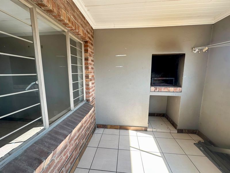 Covered patio area featuring a built-in braai, tiled flooring, and exposed brick accents, offering a functional outdoor entertainment space.