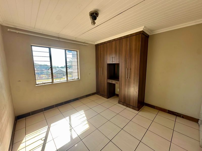A vacant bedroom featuring tiled flooring, a built-in wooden wardrobe, and a metal-framed window with natural light.