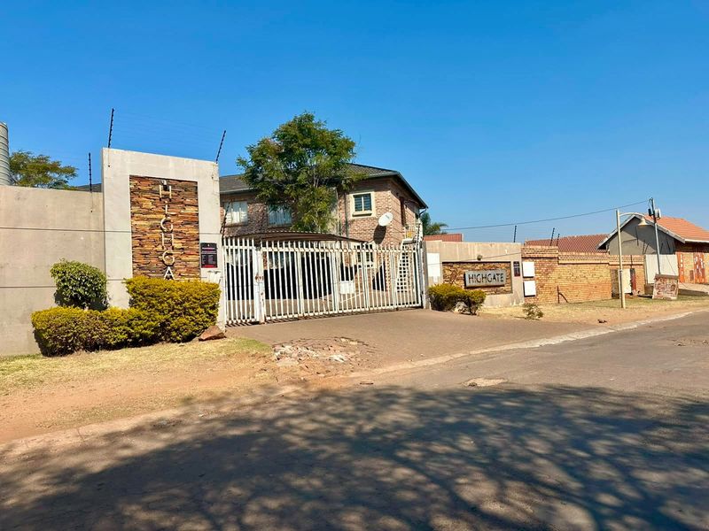 Front entrance view of Highgate apartment complex featuring a secure gated access point, brick boundary walls, and electric fencing.