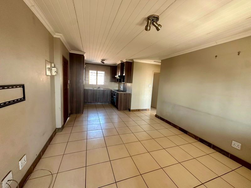 An open-plan living and kitchen area featuring tiled floors, timber-panelled ceilings, and a functional kitchen with built-in cabinetry and appliances.