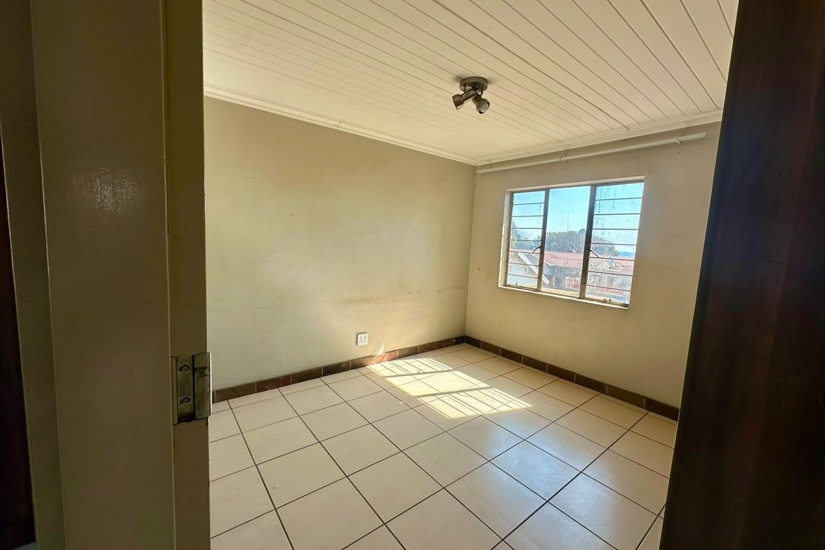 An empty bedroom featuring tiled flooring, a tongue and groove ceiling, and a steel-framed window, requiring minor cosmetic updates to the walls.
