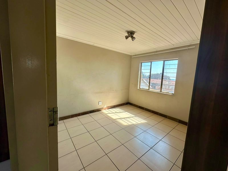 An empty bedroom featuring tiled flooring, a tongue and groove ceiling, and a steel-framed window, requiring minor cosmetic updates to the walls.