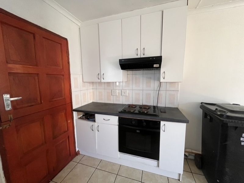 Compact kitchen featuring white cabinetry, dark laminate countertops, built-in oven, electric hob, and tiled splashback, requiring minor repairs to cabinetry and finishes.