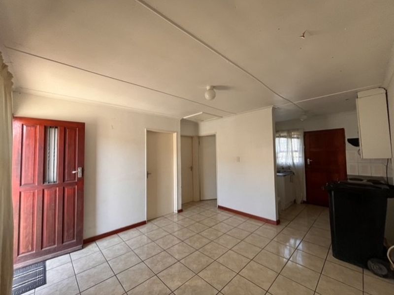 An open-plan living area featuring tiled flooring, a timber entrance door, and direct access to the kitchen and internal rooms.