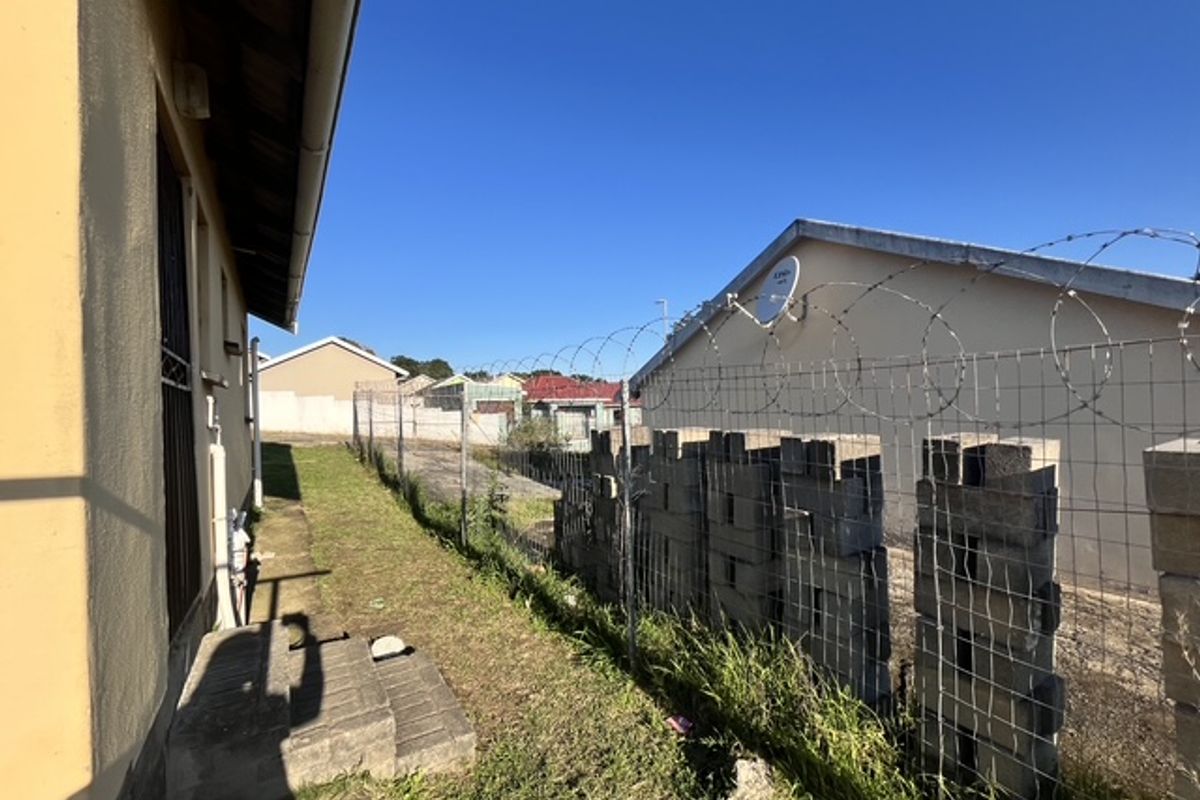 Side exterior view of the property featuring a concrete block boundary wall topped with razor wire fencing and a small concrete step area.