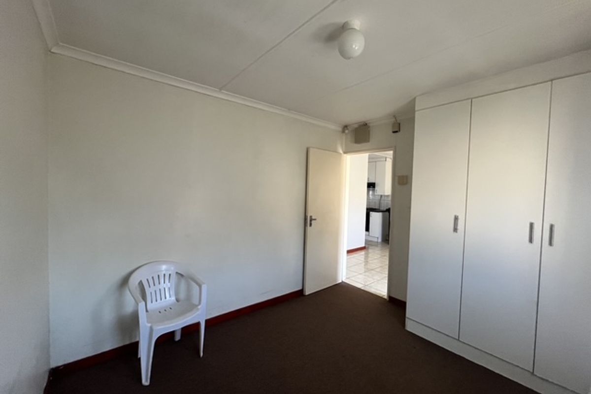 A vacant bedroom featuring built-in cupboards, carpeted flooring, and coved cornicing, with a doorway leading to an adjacent tiled area.