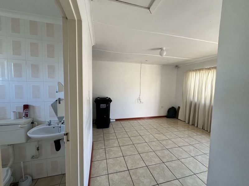 An empty open-plan living area with adjacent bathroom, featuring tiled flooring and basic fixtures, requiring cosmetic updates and minor repairs.