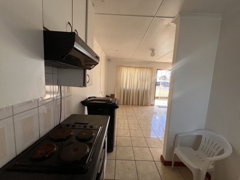 A functional kitchen area featuring tiled flooring, built-in cabinetry, and an electric hob with an extractor fan, leading into an adjacent living space.