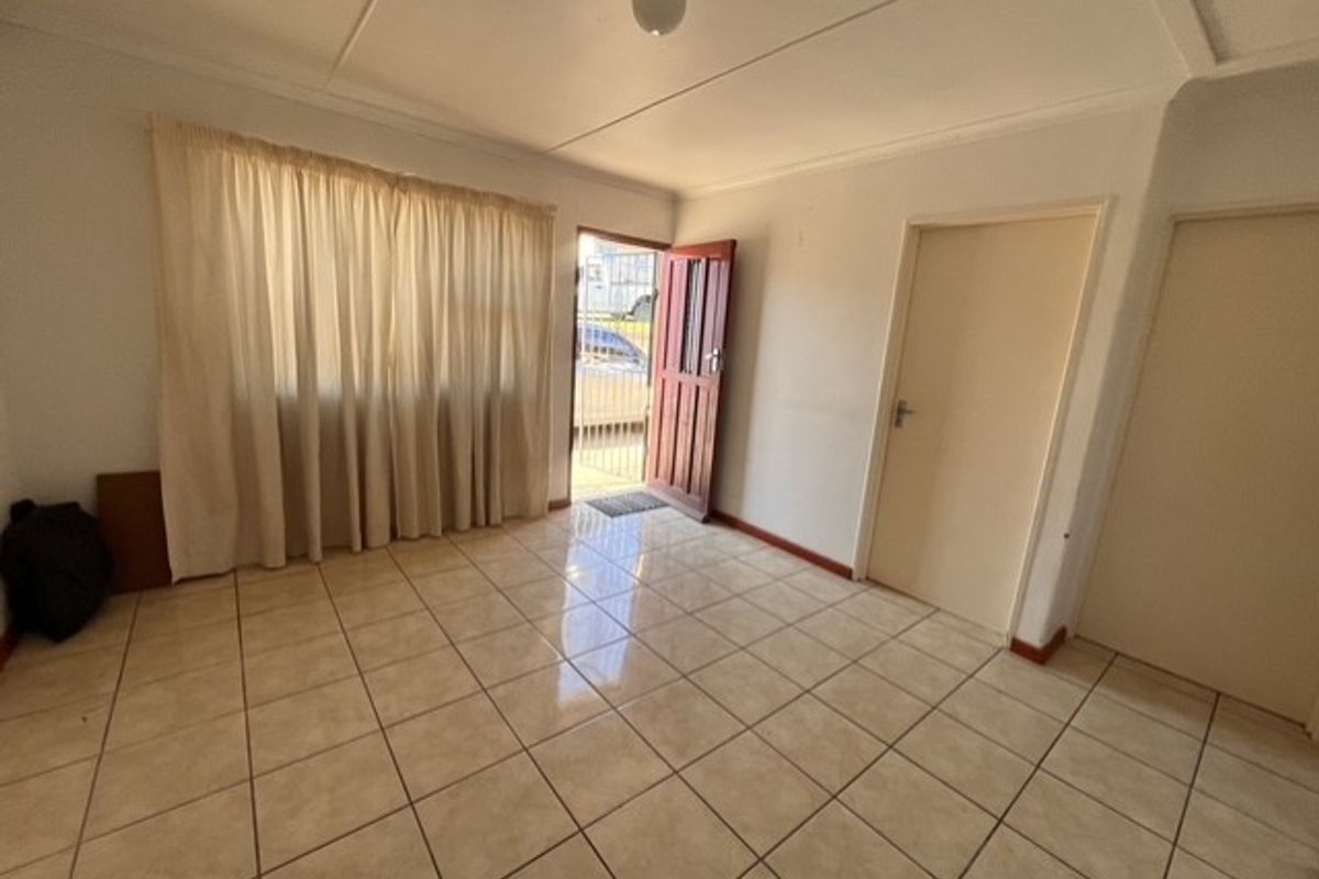 An empty living room featuring neutral tiled flooring and direct access to the exterior through a timber door with a security gate.