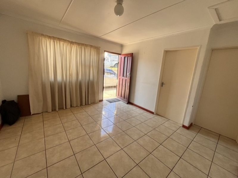 An empty living room featuring neutral tiled flooring and direct access to the exterior through a timber door with a security gate.