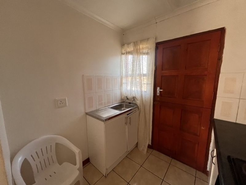 A compact scullery area featuring a stainless steel sink, tiled splashback, base cabinetry, and direct access via a timber door.
