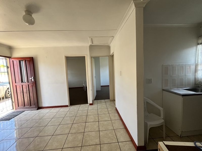 Open plan living area featuring tiled flooring, a basic kitchen sink unit with tiled splashback, and direct access to the entrance.