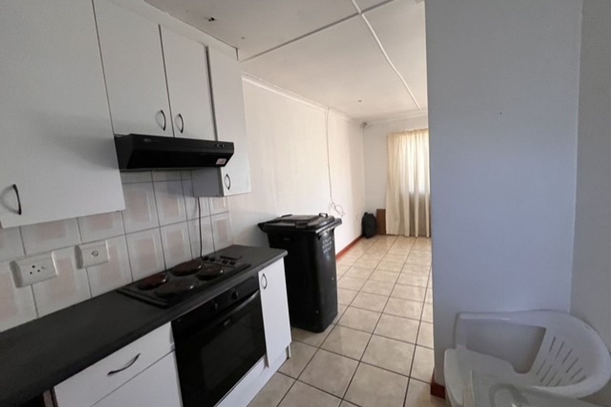 A functional kitchen area featuring built-in cabinetry, an electric hob, and oven, with tiled flooring and splashback, requiring some cosmetic attention.