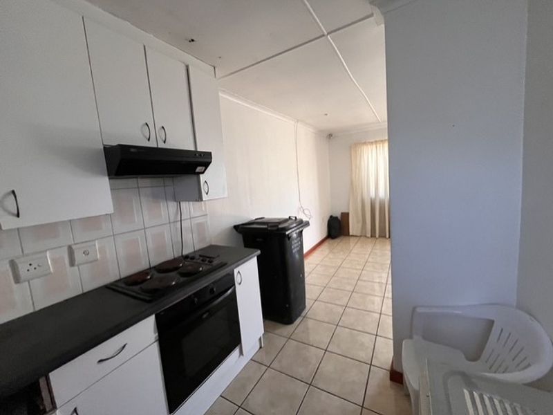 A functional kitchen area featuring built-in cabinetry, an electric hob, and oven, with tiled flooring and splashback, requiring some cosmetic attention.