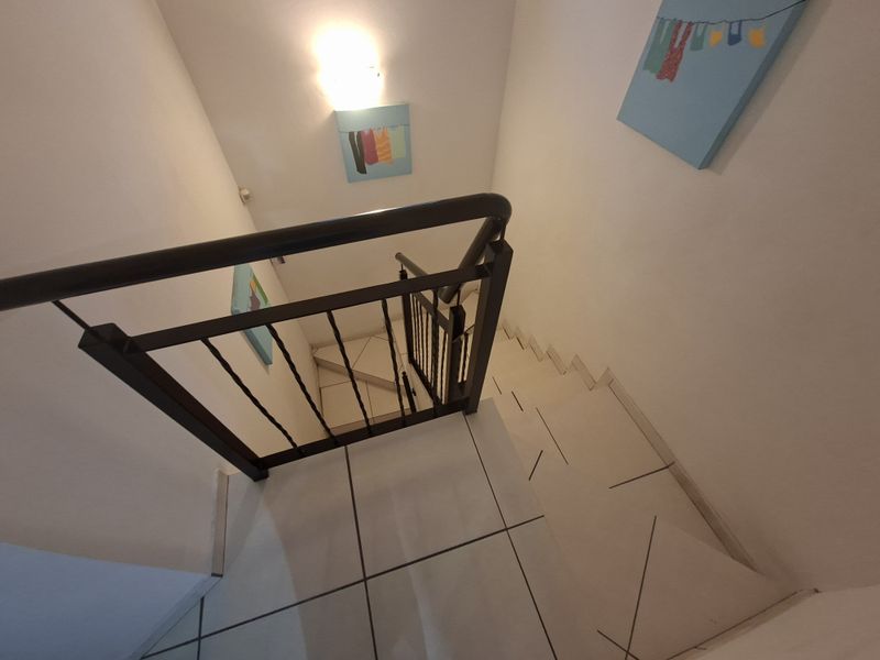 A bright, tiled staircase featuring a dark metal balustrade and wall-mounted lighting, providing access between levels in this townhouse.