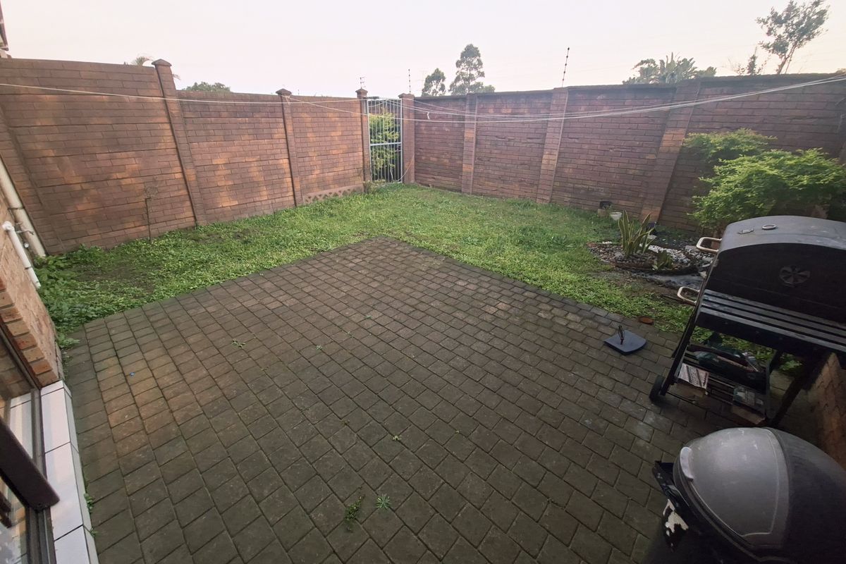 A private rear courtyard featuring a paved patio area, enclosed by high brick boundary walls with integrated electric fencing.