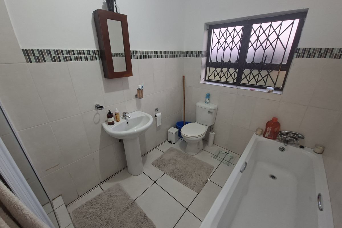 A functional bathroom featuring a pedestal basin, toilet, and bathtub with tiled finishes and security bars on the window.