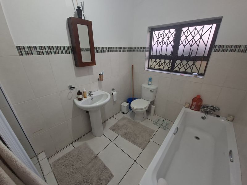 A functional bathroom featuring a pedestal basin, toilet, and bathtub with tiled finishes and security bars on the window.