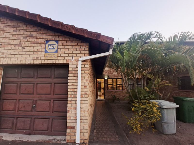 Front exterior view of a face brick townhouse featuring a single garage, paved entrance walkway, and established garden area.