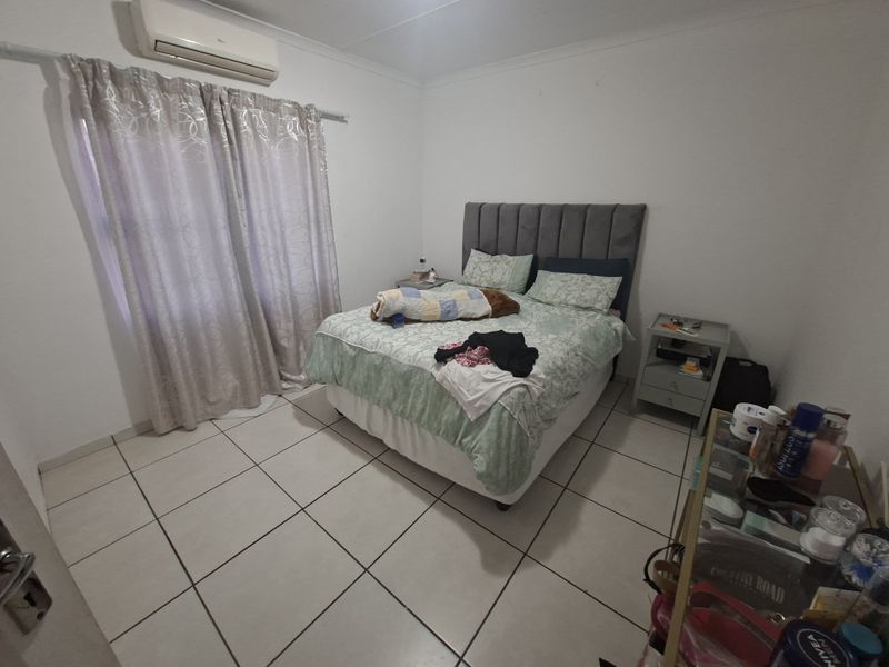 A functional bedroom featuring ceramic floor tiles, a wall-mounted split-system air conditioner, and neutral wall finishes.