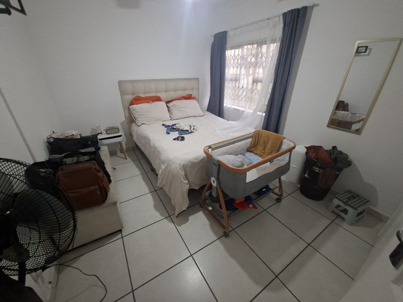 A functional bedroom featuring tiled flooring and a window fitted with a security gate, providing a practical space for rest.