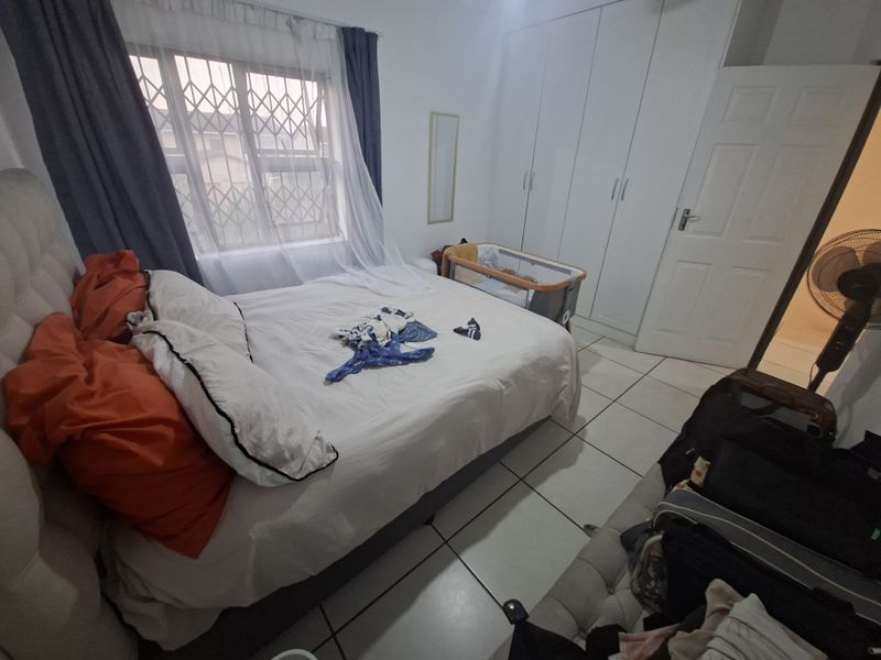 A bedroom featuring tiled flooring, built-in cupboards, and a window fitted with a security gate.