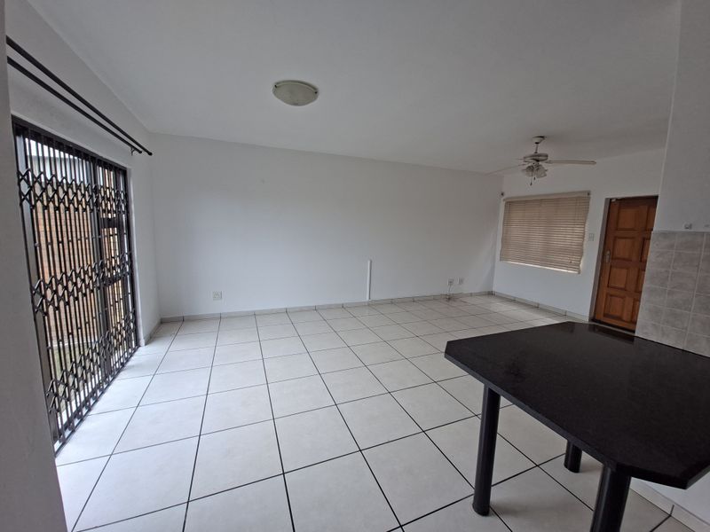 Spacious open-plan living area featuring neutral tiled flooring, a ceiling fan, and a built-in breakfast bar, offering a versatile layout for dining and relaxation.