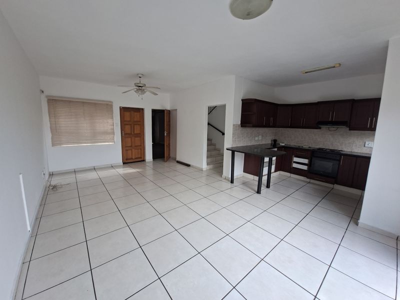 Spacious open-plan living area featuring tiled floors, a functional kitchen with dark cabinetry, breakfast bar, and direct access to the staircase.